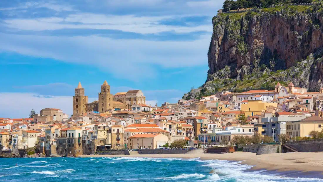 Colorful waterfront in Sicily beneath a rocky cliff